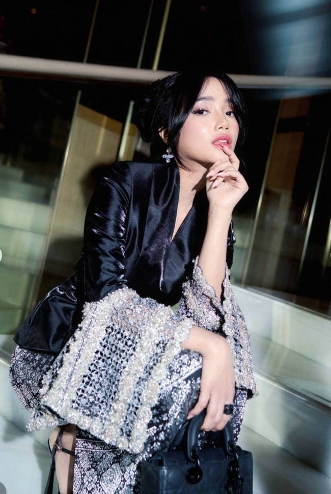 Uniknya bagian lengan busana yang dikenakan Fuji memiliki ornamen bertekstur yang melebar melingkari bagian siku hingga tangan bagian bawah. Ia juga melengkapi penampilannya dengan heels, tas, dan cincin yang juga berwarna hitam. Foto: Instagram/@fuji_an