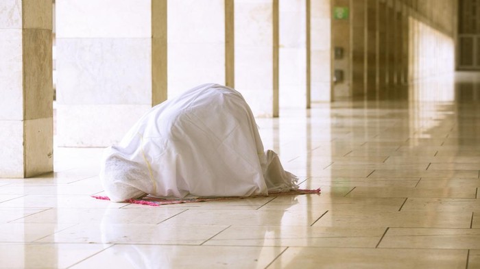 Muslim woman wearing prayer veil, doing prostration in the mosque