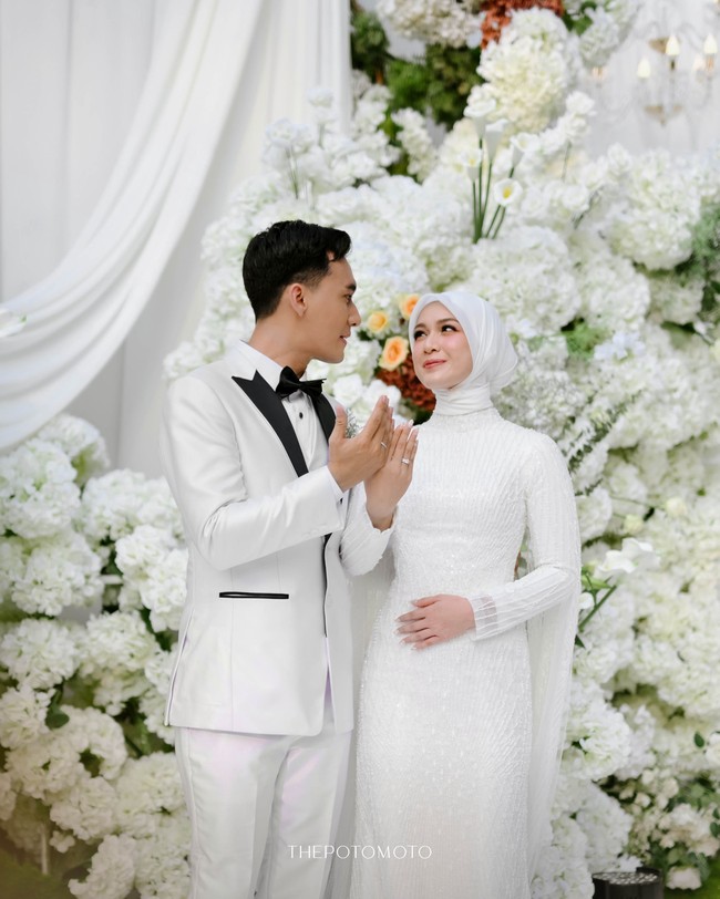 Berpose memamerkan cincin, Dea Annisa mengenakan hijab clean yang sleek, selaras dengan gaun pengantin putih yang elegan dari @irenedanielle. Gaya minimalis ini menunjukkan keanggunan seorang pengantin Muslimah modern. Foto: Dok. Instagram @deaaannisa.