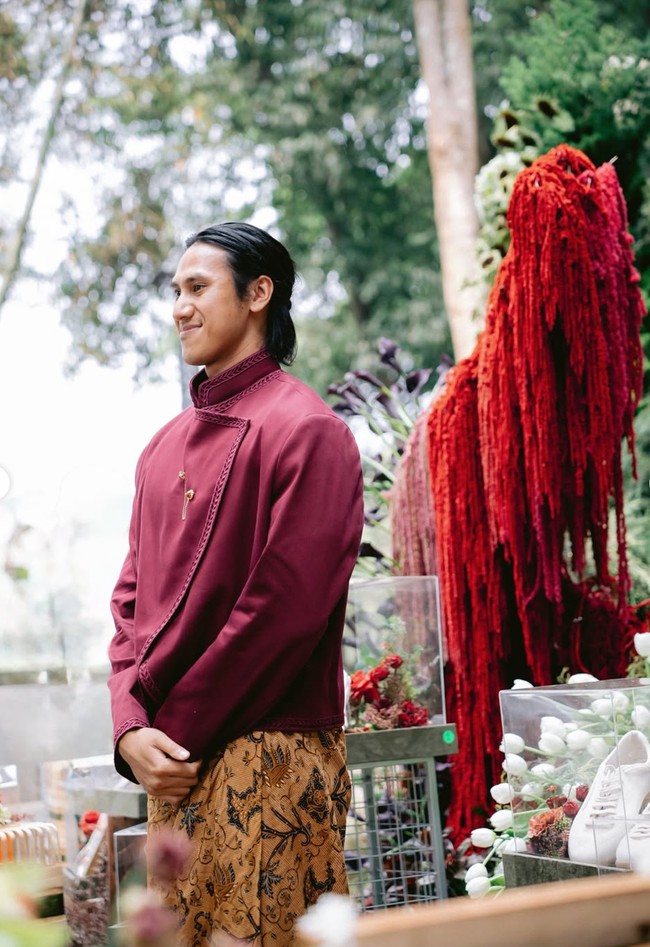 Sementara Sean mengenakan beskap modern rancangan desainer Didiet Maulana. Bagian tepi busana dihiasi detail bordir atau jahitan dekoratif yang senada, sehingga memberikan sentuhan mewah tanpa terlihat berlebihan. Sebagai bawahan, ia memakai kain batik berwarna cokelat keemasan dengan motif yang cukup ramai, memadukan unsur flora dan ornamen khas batik. Foto: Instagram/@hanamalasan