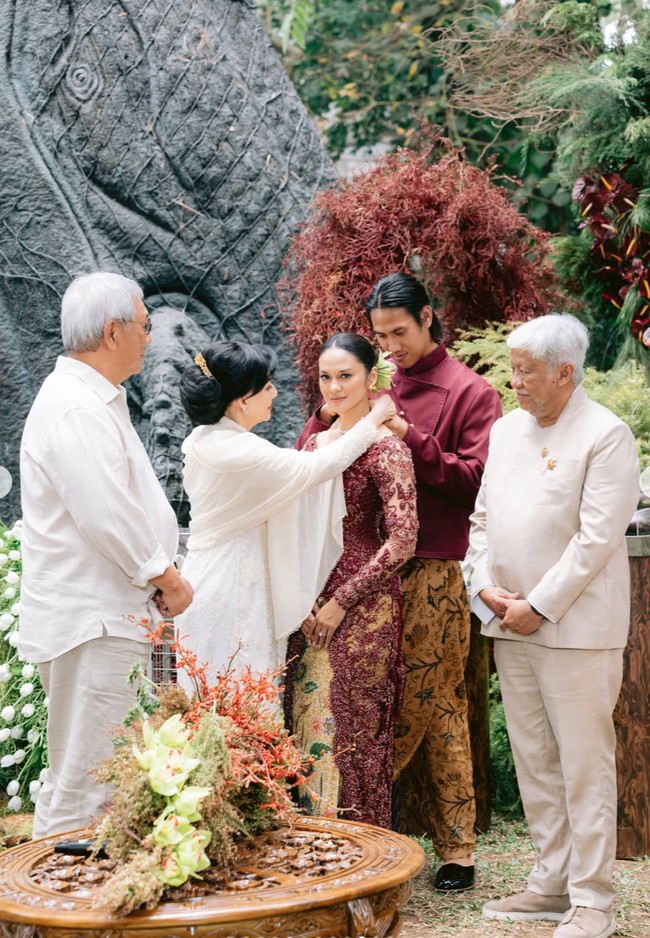 Orangtua Sean dan Hana tampil kompak dalam balutan busssana berwarna putih. Dalam foto terlihat ibunda Sean yang sedang memasangkan kalung lamaran di leher Hana. Foto: Instagram/@hanamalasan