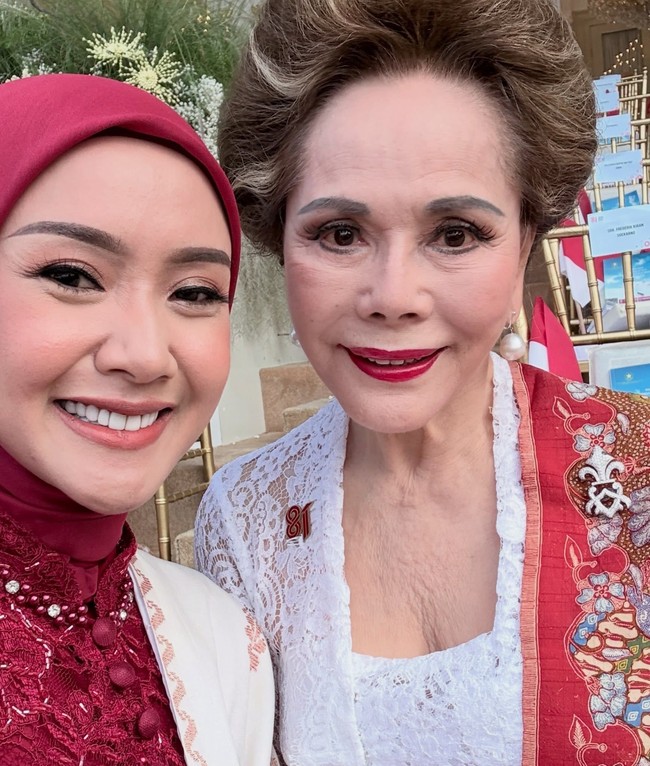 Swafoto ini memperlihatkan keharmonisan busana Cita Rahayu yang bernuansa merah-putih saat bersanding dengan Dewi Soekarno. Hijab merah marun tanpa motif dipadukan dengan kebaya brukat, memberikan kesan elegan tanpa berlebihan di samping busana kebaya putih klasik. Foto: Dok. Instagram @cita_rahayu.