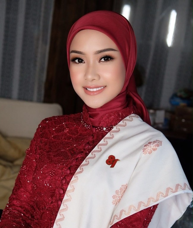 Fokus close-up memperlihatkan detail hijab segi empat merah maroon yang ditata rapi menyelimuti leher. Pin bertuliskan 81 yang disematkan pada selendang putih menjadi aksen pemanis yang menegaskan nuansa peringatan HUT RI. Foto: Dok. Instagram @cita_rahayu.