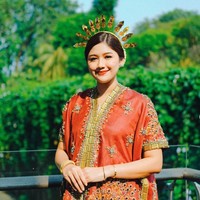 Erina mengenakan baju bodo modifikasi berpotongan longgar. Bagian depan dan tepi busana dihiasi bordiran emas yang mewah. Bagian permukaan baju ditaburi payet dan kristal. Ia juga melengkapi penampilannya dengan mahkota atau kembang goyang emas khas pakaian adat Sulawesi Selatan. Foto: Instagram/@erinagudono