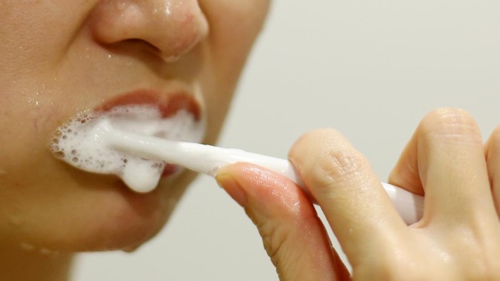 An Asian woman is enjoying brushing teeth after shower in bathroom.
