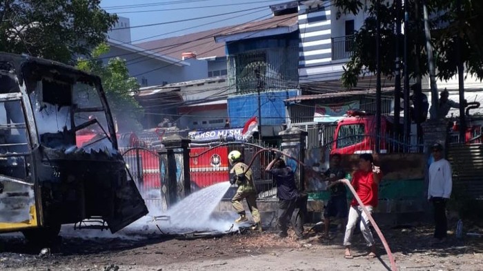 Petugas Damkarmat Makassar memadamkan api yang menghanguskan bus.