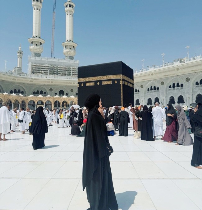 Ummi Quary tampil syari dengan balutan niqab berwarna hitam yang menutupi dada. Ia mengenakan abaya berwarna senada yang longgar dan santai saat berada di depan Kabah. Foto: Dok. Instagram @ummi_quary.