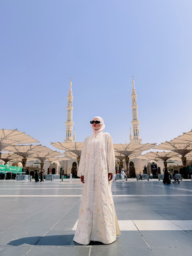 Saat berada di Madinah, Ummi Quary tampil dengan balutan outer model abaya berukuran oversize warna broken white yang beraksen bordir bunga. Penampilannya kian anggun dan manis dipadukan dengan hijab pashmina instan simpel berwarna pink soft yang dililit rapi. Foto: Dok. Instagram @ummi_quary.