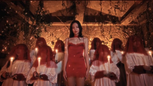 Netizen semakin geger usai melihat adegan Jennie BLACKPINK berbalut gaun satin merah. Berdiri di tengah kumpulan anak-anak yang memakai tudung kepala, kostum putih menyerupai busana misdinar gereja, sambil memegang lilin. Foto: dok. YouTube JENNIE