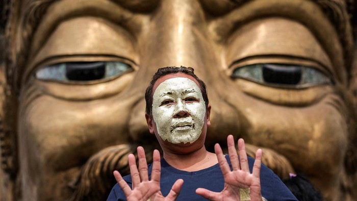 Devotees with their faces covered in gold leaves pose for a picture in front of a statue of Por Kae during a 