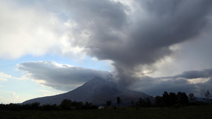 Warga mengendarai sepeda motor dengan latar Gunung Sinabung yang erupsi di Kecamatan Naman Teran, Kabupaten Karo, Sumatera Utara, Senin (31/8/2026). Gunung Sinabung mengalami erupsi dengan tinggi kolom abu mencapai 3.500 meter atau sekitar 5.960 mete