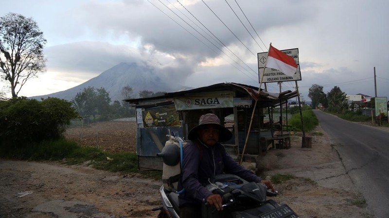 Warga mengendarai sepeda motor dengan latar Gunung Sinabung yang erupsi di Kecamatan Naman Teran, Kabupaten Karo, Sumatera Utara, Senin (31/8/2026). Gunung Sinabung mengalami erupsi dengan tinggi kolom abu mencapai 3.500 meter atau sekitar 5.960 meter di atas permukaan laut.ANTARA FOTO/Yudi Manar