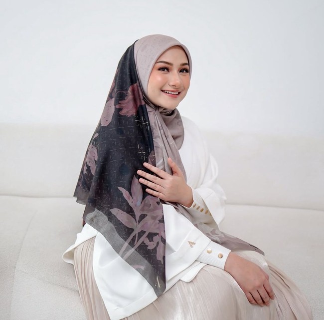 Gaya feminin ala Nadzira terlihat manis lewat paduan atasan putih dan hijab bermotif bunga bernuansa gading serta cokelat pastel. Rok plisket bernuansa senada melengkapi penampilannya yang memberikan kesan lembut dan bersahaja. Foto: Dok. Instagram @enazirashf_.
