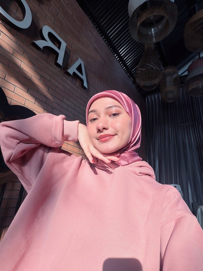 Gaya santai ala streetwear ditampilkan lewat perpaduan hoodie merah muda dengan hijab segi empat bahan satin bernuansa senada. Efek kilap dari hijab satin memberikan sentuhan manis dan trendi pada pakaian kasualnya. Foto: Dok. Instagram @enazirashf_.