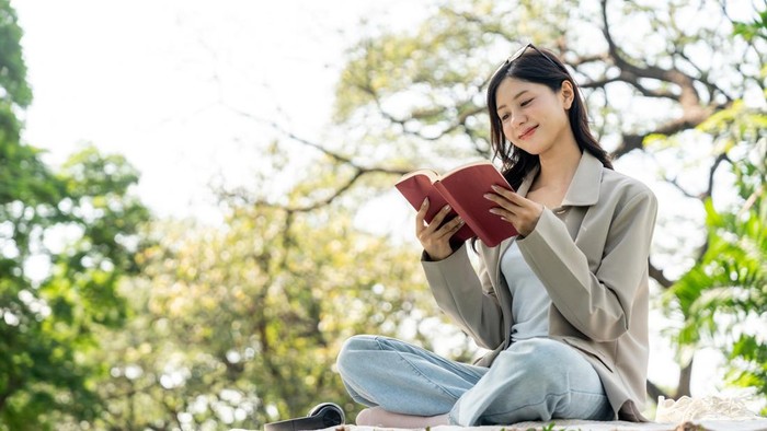 Young asian woman relaxing reading book sitting at public park life style outdoor. Happy female Take a break enjoy time living in the nature. Human and nature together