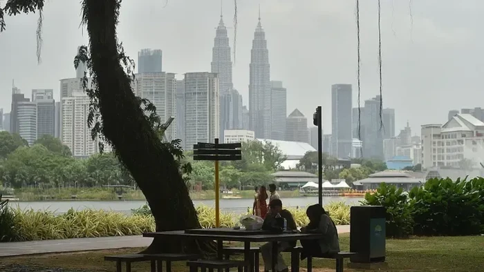 Pengunjung taman duduk di tepi danau dan Menara Kembar Petronas (tengah), ikon Kota Kuala Lumpur, tampak tertutup kabut asap