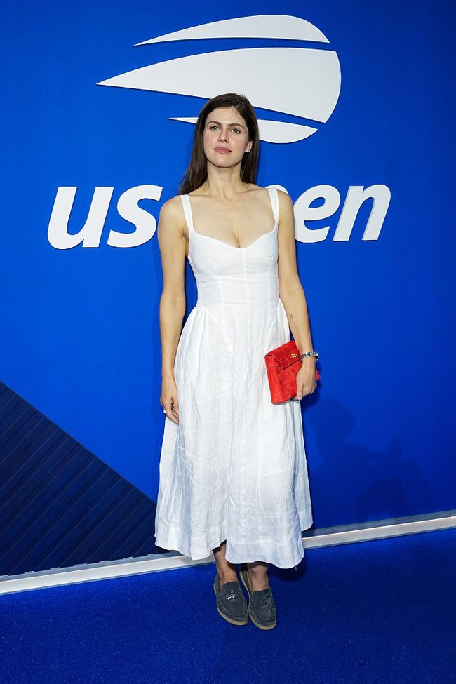 Aktris Alexandra Daddario memilih pendekatan yang lebih feminin dan klasik lewat little white dress.  Untuk menghindari tampilan serba putih yang terlalu polos, ia menambahkan clutch merah sebagai aksen warna. Sepasang loafers bernuansa abu-abu gelap membuat penampilannya terasa lebih santai dan modern. Foto: Getty Images/John Nacion