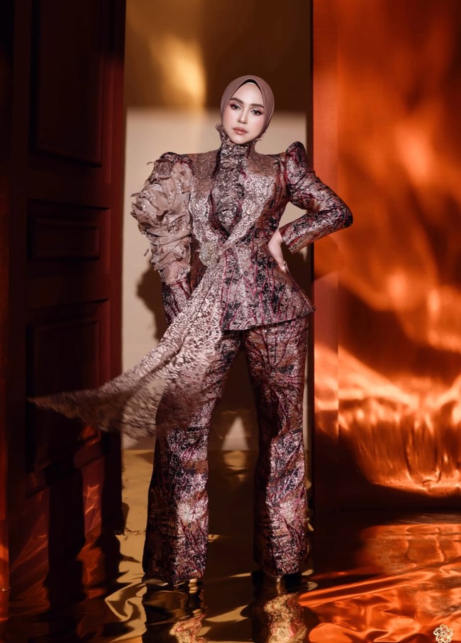 Ricis mengenakan setelan bernuansa cokelat maroon, dusty rose, dan keemasan dengan motif yang terlihat mewah. Atasannya berpotongan peplum, sehingga bagian pinggang tampak lebih tegas sementara bagian bawah sedikit mengembang. Foto: Instagram/@riaricis1795
