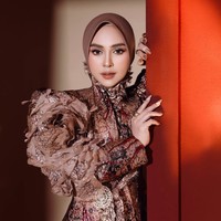 Bagian paling mencolok adalah lengan kiri yang dibuat sangat bervolume dengan susunan ruffle atau layer kain bertumpuk. Atasannya juga memiliki model kerah tinggi dengan aksen kain yang tampak seperti ruffle atau drapery di area leher dan dada. Foto: Instagram/@riaricis1795