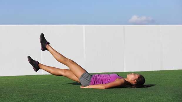 Fitness woman training abs workout doing scissor lifts leg raise or flutter kicks exercise out outdoor grass floor at gym.