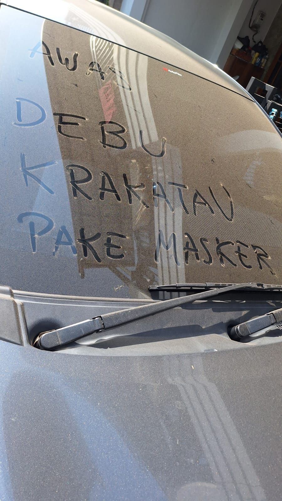Sebuah mobil terlihat dengan tulisan “Awas Debu Krakatau, Pakai Masker” yang dibuat menggunakan debu vulkanik yang menempel pada kaca kendaraan akibat paparan erupsi Gunung Anak Krakatau. (Dok. Istimewa)