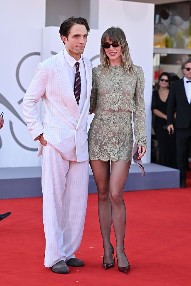 Seperti dikutip Vogue, Robert Pattinson dan Suki Waterhouse menebarkan pesona mereka di karpet merah Festival Film Venesia 2026. Pattinson mengenakan setelan jas kustom Dior Homme berwarna serba putih dengan motif pinstripe halus, yang ia padukan dengan kemeja putih, dasi garis-garis warna biru dongker dan merah, serta sepatu loafers cokelat. Foto: Dok. Getty Images, Wireimages