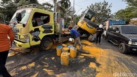 Akibatnya, ekskavator yang diangkut bergeser dan sebagian jatuh dari bak truk. Sejumlah tong cat berwarna oranye yang ikut diangkut juga tumpah ke aspal.