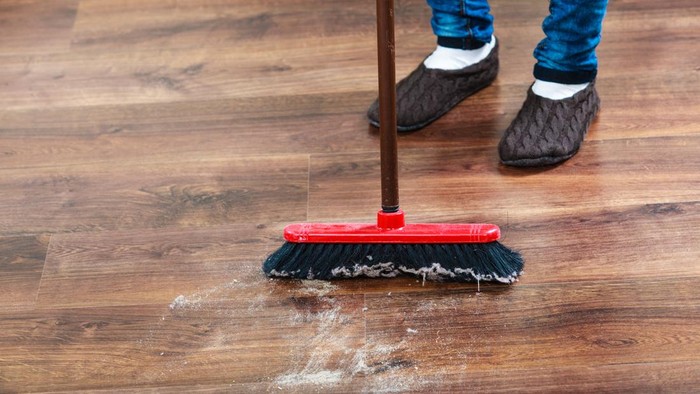 Cleanup housework concept. Closeup broom and female foots. Cleaning woman sweeping wooden floor.