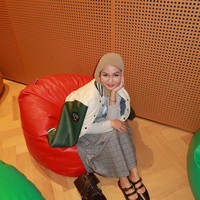 Xaviera Putri memakai pashmina cokelat muda dengan penataan melingkar rapi di kepala. Tampilan outfit bergaya preppy casual memadukan kemeja, rok plisket kotak-kotak, serta jaket varsity kombinasi krem-hijau. Foto: Dok. Instagram @xavieraaputri.