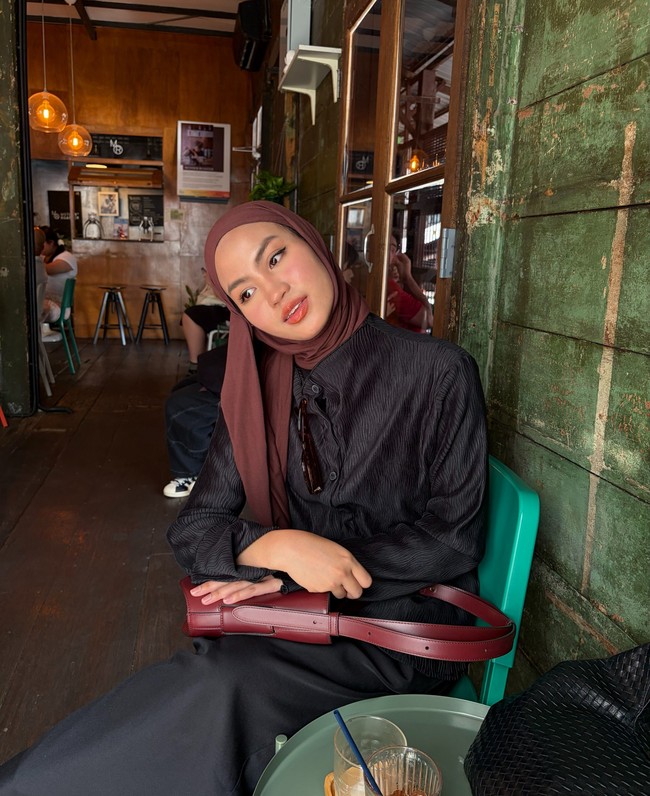 Kali ini, Xaviera menggunakan pashmina cokelat tua bernuansa bold yang salah satu sisinya dibiarkan menjuntai ke depan. Padu padan outfit berupa atasan hitam textured dan rok senada yang dilengkapi tas bahu merah bata untuk memberi aksen warna matching. Foto: Dok. Instagram @xavieraaputri.