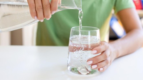 Unrecognizable female pouring clean drinking water from jug into glass