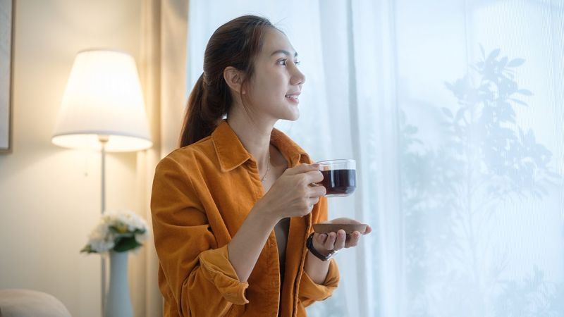 Smiling young woman holding a cup of coffee and gazing out the window.