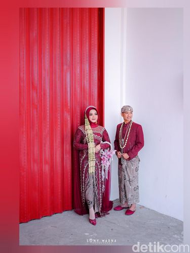Pasangan pengantin Alifah dan Erwan tampil unik dengan berfoto di depan gedung Koperasi Desa Bulurejo usai resepsi, berbalut busana merah marun yang serasi.