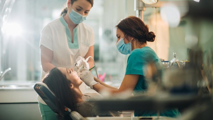 Young woman having her teeth checked by two dentist during appointment at dentist office.