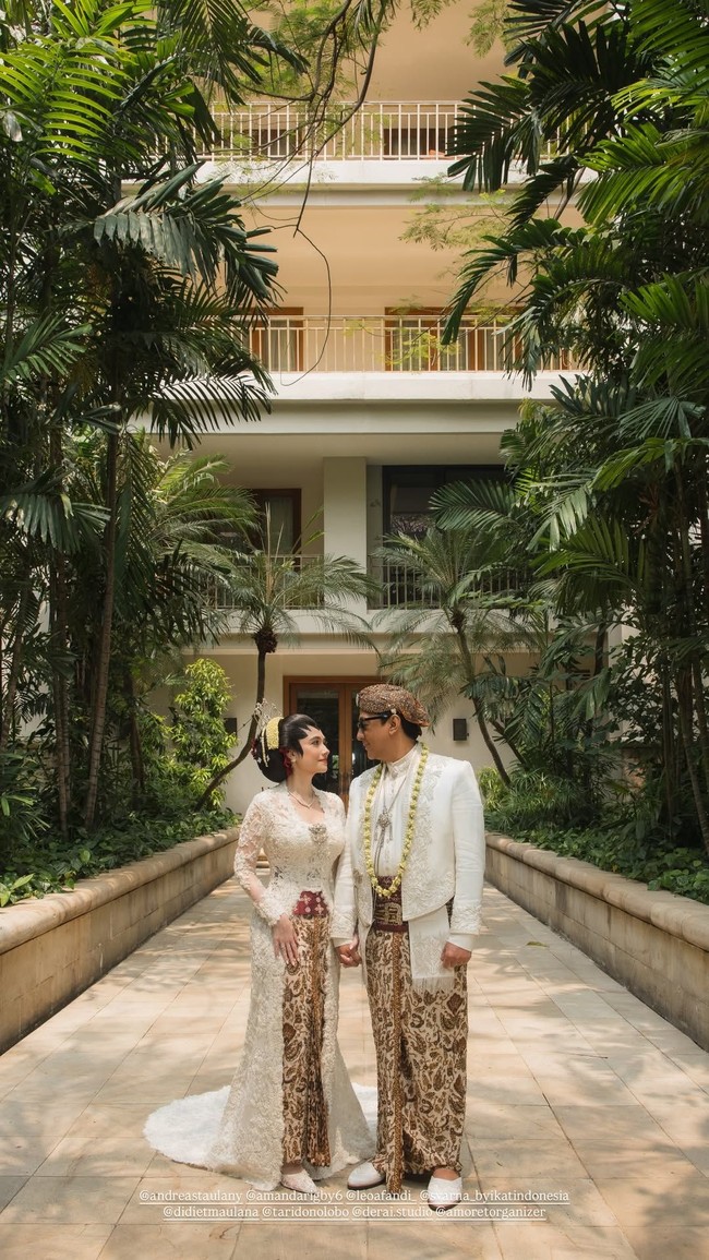 Amanda Rigby dan Andre Taulany tampil menjadi pengantin Jawa dalam balutan kebaya dan beskap putih yang dipadukan kain batik palet putih-cokelat. Sentuhan stagen warna merah marun memberikan aksen kontras pada penampilan Amanda. Foto: Dok. Instagram Didiet Maulana, Amoretorganizer