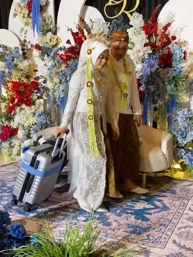 Suasana pengantin membawa koper saat di pelaminan bikin warganet salah fokus. Suasana pengantin membawa koper saat di pelaminan bikin warganet salah fokus.