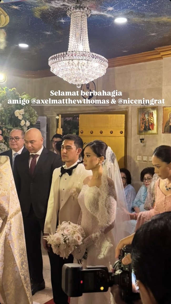 Tampil serasi, Axel dan Cicilia kenakan busana pengantin bernuansa putih. Axel sendiri tampak mengenakan kemeja dan jas putih dipadukan ceelana panjang dan dasi kupu-kupu hitam. Foto: Instagram/@axelmatthewthomas