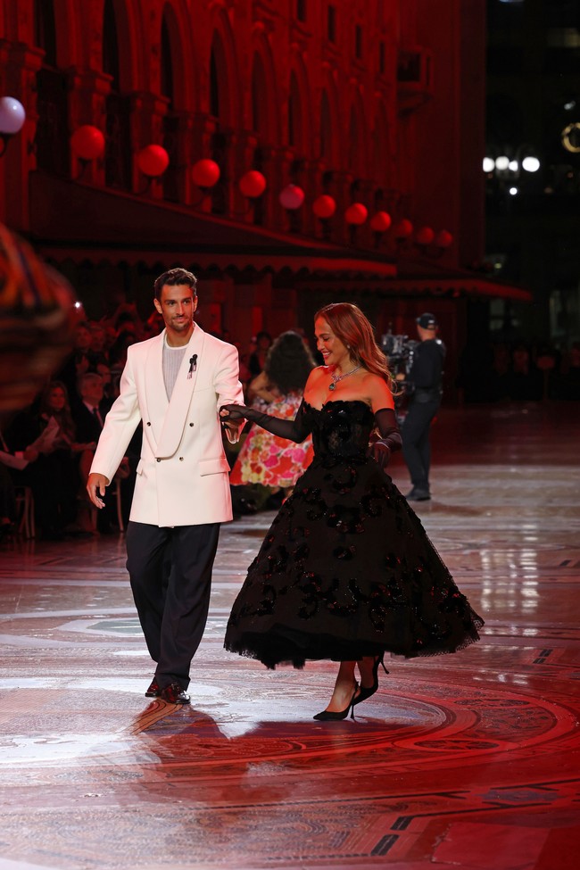 J.Lo berbagi runway dengan Lorenzo Musetti, petenis muda asal Italia yang tampil elegan dalam setelan jas oversized dan celana hitam. Keduanya tampak berdansa dan bergandengan tangan. Foto: Getty Images for Vogue/Stefania M. DAlessandro