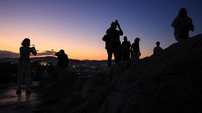 Tourists enjoy the moon and sunset views near the Acropolis, during the first autumn day, at the Areopagus Hill in Athens, Greece, September 23, 2026. REUTERS/Louisa Gouliamaki