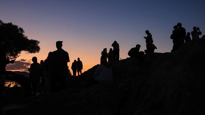 Tourists enjoy the moon and sunset views near the Acropolis, during the first autumn day, at the Areopagus Hill in Athens, Greece, September 23, 2026. REUTERS/Louisa Gouliamaki