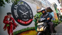 Pesepeda motor melewati mural bergambar silat cingkrik di Kampung Betawi Rawa Belong. Rawa Belong yang juga merupakan desa wisata kampung silat yang ada di Jakarta telah melaksanakan festival silat berskala besar. Pada 2019 lalu sekitar 1.000 pendekar tumpah ruah di area dekat Pasar Bunga Rawa Belong itu.
