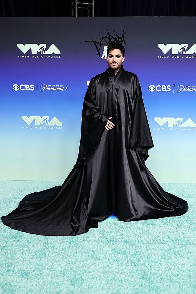 Penyanyi Adam Lambert hadir di VMA 2026 untuk tampil dalam tribute bagi George Michael dengan mengenakan busana custom Charles de Vilmorin. Jubah hitam bergaya gothic dengan lengan mengembang dipadukan dengan headpiece bertuliskan Adam’. Luarannya polos tanpa detail menarik membuat gaya Adam terasa membosankan.  Foto: Getty Images/Frazer Harrison