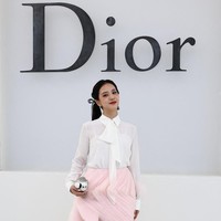 Jisoo mengenakan blouse putih transparan dengan detail pita panjang yang dipadukan dengan rok mini berwarna powder pink. Rok tersebut merupakan bagian dari koleksi Dior Spring-Summer 2027 dan memiliki permainan layering serta draping yang memberikan volume lembut pada siluet. (Foto: REUTERS/Sarah Meyssonnier)