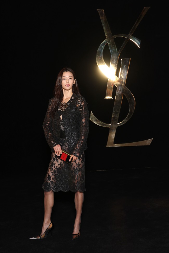 Sebagai wajah baru Saint Laurent, Jun Ji Hyun tampil memakai silicone-lace cropped jacket, yang dipadukan dengan tank top dan pencil skirt senada. Clutch emas dengan aksen logo Saint Laurent menambah kesan mewah. Foto: Getty Images