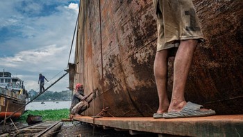 Foto ini mendapat pujian kategori Travel. Pada tanggal 14 Agustus 2025 di Dhaka, Bangladesh, pemandangan di halaman industri tepi sungai ini menunjukkan aktivitas di sekitar lambung kapal besar. Gambar ini menangkap suasana keras dari pekerjaan manual yang berat. Saya mengambil foto ini untuk mendokumentasikan skala, tekstur, dan intensitas lingkungan perbaikan kapal. 
