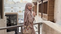 Niken Anjani tampak bersantai dengan menggenggam segelas minuman dingin. Ia berpose di area selasar dengan latar belakang kemegahan menara Masjidil Haram. Mekah dalam hatiku, tulisnya. (Foto: dok Instagram nikenanjanii)