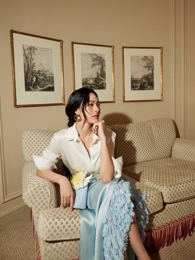 Lingling Kwong tampil mencuri perhatian mengenakan kemeja putih berkerah dengan lengan yang digulung hingga siku dan rok satin biru muda yang dihiasi aksen motif bunga dan detail pita putih. Foto: Dok. Instagram Lingling Kwong, Orm Kornnaphat