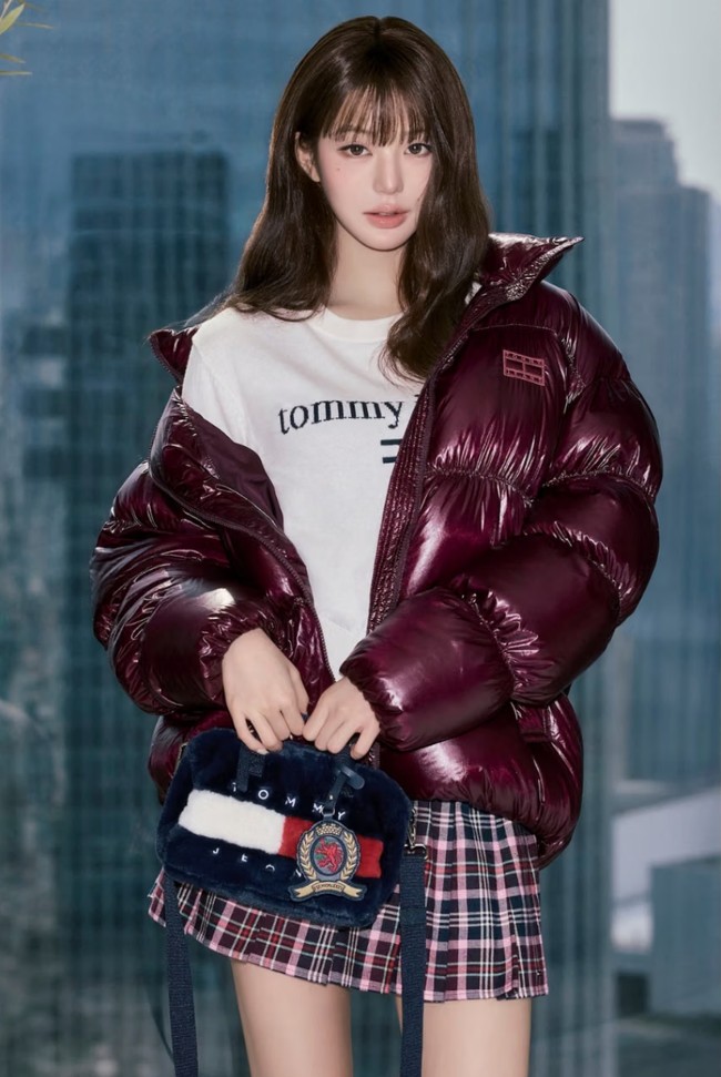 Kampanye ini menampilkan Wonyoung yang memadukan elemen gaya klasik dengan sentuhan unik tak terduga. Dalam salah satu tampilan, ia mengenakan rok lipit tartan bergaya preppy dengan sweater oversized, jaket puffer mengilap, serta tas micro duffle beraksen bulu yang mewah. Foto: Dok. Tommy Hilfiger