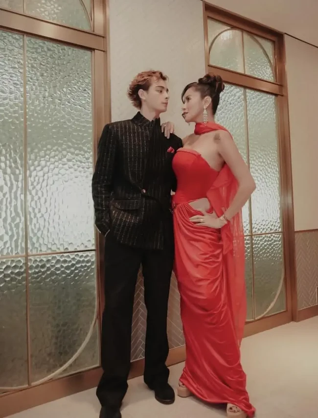 Olla tampil mencuri perhatian dalam balutan gaun satin merah tanpa tali dengan detail potongan di pinggang dan selendang sifon. Tristan memadukannya dengan jas hitam berkerah tegak yang dihiasi motif garis emas. Sapu tangan saku merah marun membuat penampilan keduanya semakin serasi dan glamor. Foto: Instagram/@ollaramlan
