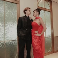 Olla tampil mencuri perhatian dalam balutan gaun satin merah tanpa tali dengan detail potongan di pinggang dan selendang sifon. Tristan memadukannya dengan jas hitam berkerah tegak yang dihiasi motif garis emas. Sapu tangan saku merah marun membuat penampilan keduanya semakin serasi dan glamor. Foto: Instagram/@ollaramlan